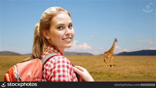 adventure, travel, tourism, hike and people concept - smiling young woman with backpack over giraffe in african savannah background. happy woman with backpack over african savannah. happy woman with backpack over african savannah