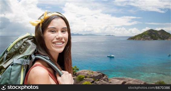 adventure, travel, tourism, hike and people concept - smiling young woman with backpack over background of seychelles island in indian ocean. happy woman with backpack over seychelles island. happy woman with backpack over seychelles island