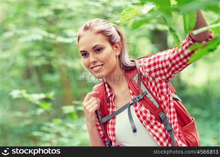 adventure, travel, tourism, hike and people concept - smiling young woman with backpack hiking in woods