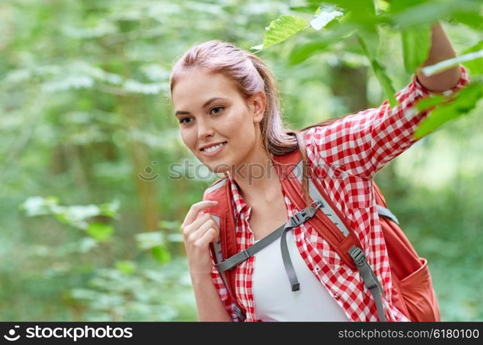 adventure, travel, tourism, hike and people concept - smiling young woman with backpack hiking in woods