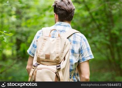 adventure, travel, tourism, hike and people concept - young man with backpack hiking in woods from back