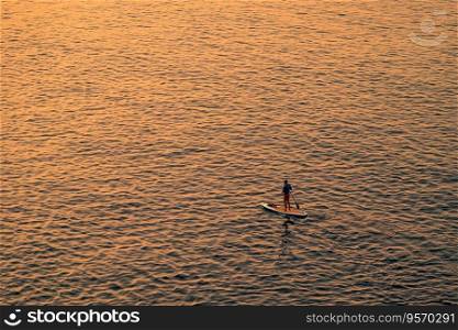 Adventurous people on a stand up paddle board is paddling during a bright and vibrant sunrise