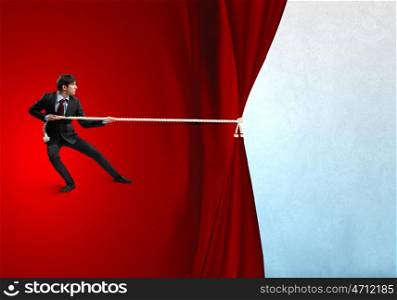 Advertise concept. Young businessman pulling curtain with rope. Place for text