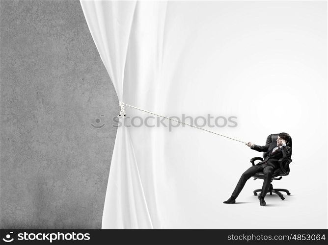 Advertise concept. Young businessman sitting in chair and pulling curtain with rope