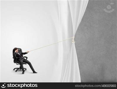 Advertise concept. Young businessman sitting in chair and pulling curtain with rope