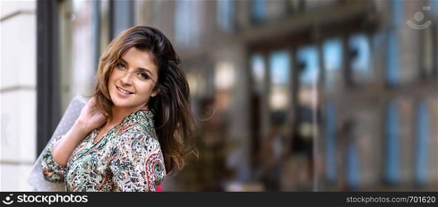 Advertisement banner - happy young woman with shopping bags is looking at camera and smiling while doing shopping in the city ( copy space)