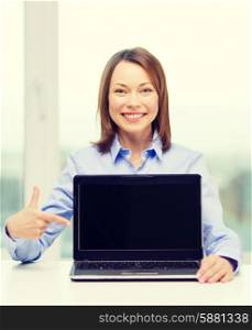 advertisement, business and technology concept - smiling businesswoman pointing finger to blank black laptop screen