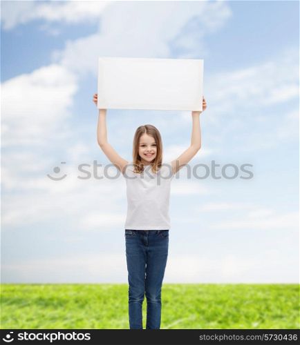 advertisement, childhood, happiness and people concept - smiling little child in white t-shirt holding blank board over blue sky and grass background