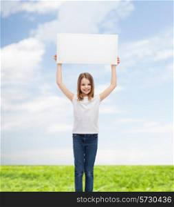 advertisement, childhood, happiness and people concept - smiling little child in white t-shirt holding blank board over blue sky and grass background