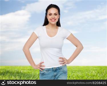 advertisement, clothing and people concept - happy smiling young woman or teenage girl in white t-shirt over blue sky and grass background