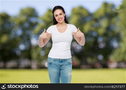 advertisement, clothing and people concept - happy smiling young woman or teenage girl in white t-shirt pointing finger to herself over summer park background