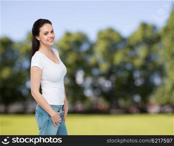 advertisement, clothing and people concept - happy smiling young woman or teenage girl in white t-shirt over summer park background