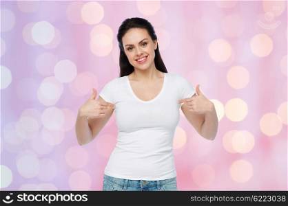 advertisement, clothing and people concept - happy smiling young woman or teenage girl in white t-shirt pointing finger to herself over rose quartz and serenity holidays lights background