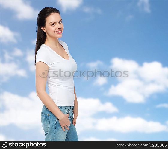 advertisement, clothing and people concept - happy smiling young woman or teenage girl in white t-shirt over blue sky and clouds background