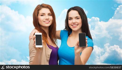 advertisement, cloud computing, people and modern technology concept - two smiling teenage girls or young women showing blank smartphones screens over blue sky with clouds background
