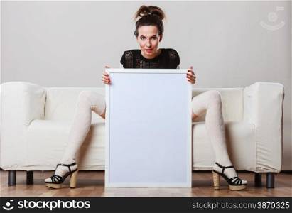 Advertisement concept. Fashionable woman sitting on sofa with blank presentation board. Female model showing banner sign billboard copy space for text.