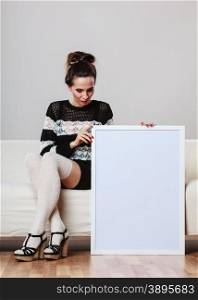 Advertisement concept. Fashionable woman sitting on sofa with blank presentation board. Female model showing banner sign billboard copy space for text.