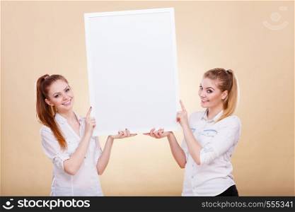 Advertisement concept. Teenage smiling girls holding blank presentation board. Young women showing banner sign billboard copy space for text. Two girls with blank presentation board
