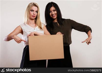 Advertisement concept. Two women caucasian and african with blank board empty banner pointing with finger studio shot