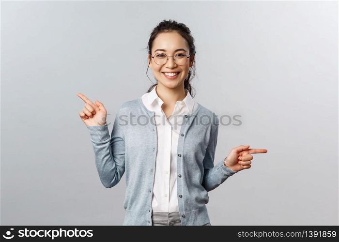 Advertisement, education and people concept. Girl recommends both products. Cheerful young asian woman in glasses pointing sideways, showing left and right promo with pleased smile.. Advertisement, education and people concept. Girl recommends both products. Cheerful young asian woman in glasses pointing sideways, showing left and right promo with pleased smile