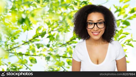 advertisement, education, ethnicity, vision and people concept - happy smiling young african woman or teenage student girl in eyeglasses and white t-shirt over green natural background
