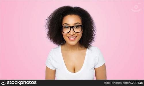advertisement, education, ethnicity, vision and people concept - happy smiling young african woman or teenage student girl in eyeglasses and white t-shirt over pink background