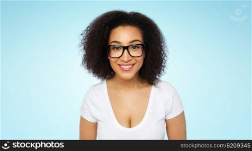 advertisement, education, ethnicity, vision and people concept - happy smiling young african woman or teenage student girl in eyeglasses and white t-shirt over blue background