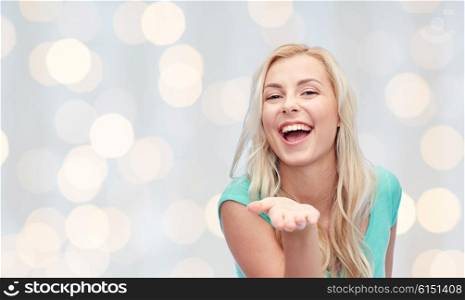 advertisement, emotions and people concept - smiling young woman or teenage girl holding something on hand over holidays lights background