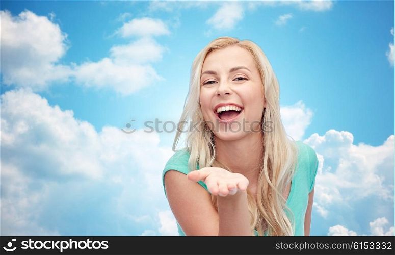 advertisement, emotions and people concept - smiling young woman or teenage girl holding something on hand over blue sky and clouds background