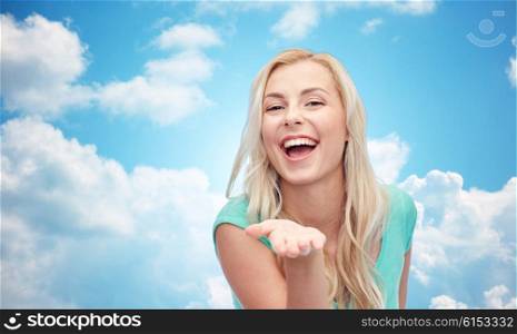 advertisement, emotions and people concept - smiling young woman or teenage girl holding something on hand over blue sky and clouds background