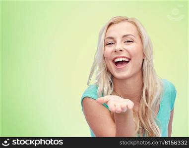 advertisement, emotions and people concept - smiling young woman or teenage girl holding something on hand over green natural background