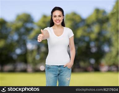 advertisement, gesture, clothing and people concept - happy smiling young woman or teenage girl in white t-shirt showing thumbs up over summer park background