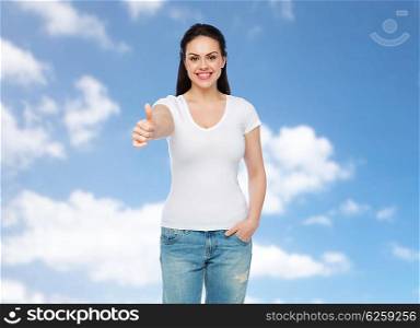 advertisement, gesture, clothing and people concept - happy smiling young woman or teenage girl in white t-shirt showing thumbs up over blue sky and clouds background