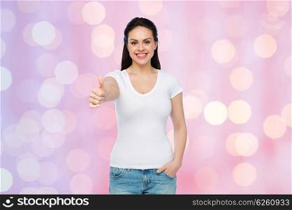 advertisement, gesture, clothing and people concept - happy smiling young woman or teenage girl in white t-shirt showing thumbs up over rose quartz and serenity holidays lights background