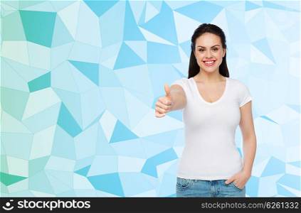 advertisement, gesture, clothing and people concept - happy smiling young woman or teenage girl in white t-shirt showing thumbs up over blue low poly background