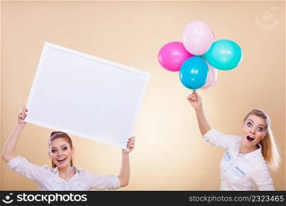 Advertisement, holidays celebration concept. Smiling joyful girls holding presentation board, banner sign and colorful balloons, having fun. Two girls with blank board and balloons