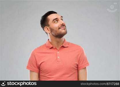 advertisement, idea, inspiration and people concept - happy smiling young man in polo t-shirt looking up over gray