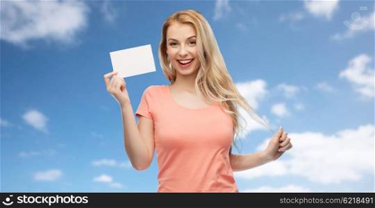 advertisement, invitation, message and people concept - smiling young woman or teenage girl with blank white paper card over blue sky and clouds background