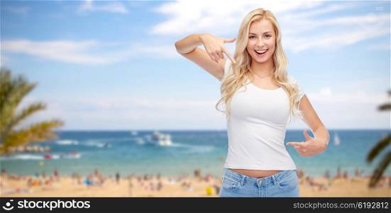 advertisement, summer holidays, travel and people concept - happy smiling young woman or teenage girl in white t-shirt pointing finger to herself over exotic tropical beach and sea background