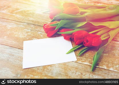 advertisement, valentines day, greeting and holidays concept - close up of red tulips and blank paper or letter on wooden background