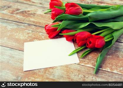 advertisement, valentines day, greeting and holidays concept - close up of red tulips and blank paper or letter on wooden background