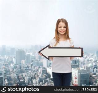 advertising and child concept - smiling little girl with blank arrow pointing left