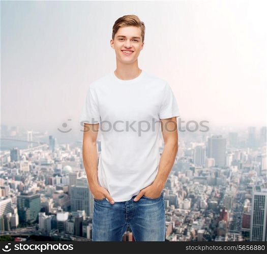 advertising and people concept - smiling young man in blank white t-shirt over city background