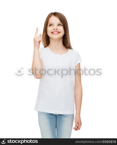 advertising and t-shirt design concept - smiling little girl in white blank t-shirt over white background pointing finger up