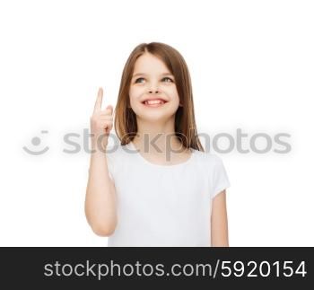 advertising and t-shirt design concept - smiling little girl in white blank t-shirt over white background pointing finger up. smiling little girl in white blank t-shirt