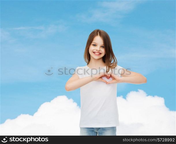 advertising, charity, childhood and people - smiling little girl in white blank t-shirt making heart-shape gesture over blue sky background