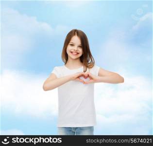 advertising, charity, childhood and people - smiling little girl in white t-shirt t making heart-shape gesture over cloudy sky background