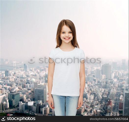 advertising, childhood and people concept - smiling little girl in white blank t-shirt over city background
