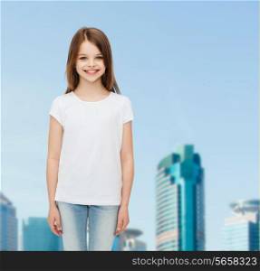 advertising, childhood, city and people concept - smiling little girl in white blank t-shirt over business center background