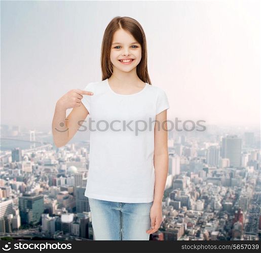 advertising, childhood, gesture and people concept - smiling little girl in white t-shirt pointing finger on herself over city background